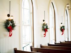 two wreaths hanging on the wall above pews in a church with arched windows