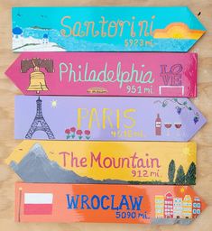 four different colored wooden signs with the names of cities and towns painted on each one