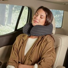 a woman sitting in the back seat of a car with her head resting on a pillow