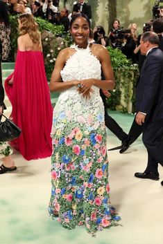 a woman in a floral dress standing on a green carpet with cameras around her and people behind her