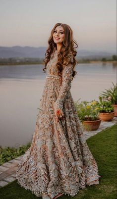 a woman standing in front of a body of water wearing a dress with long sleeves