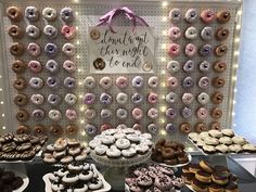 a table topped with lots of donuts next to a wall covered in frosting