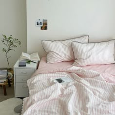 a bed with pink sheets and pillows in a bedroom next to a small table, potted plant