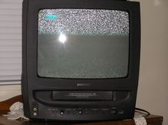 an old tv sitting on top of a wooden table next to a window with blinds