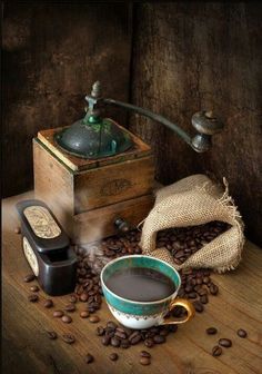 a cup of coffee sitting on top of a table next to a grinder and beans