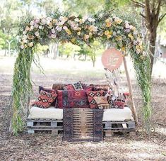 an outdoor seating area with pillows and flowers on the bench, surrounded by greenery