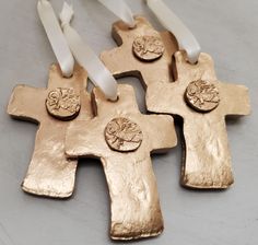 four gold crosses with white ribbons hanging from the side on a gray surface, in front of two candles