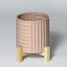 a small pink vase sitting on top of a wooden stand in front of a gray background