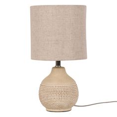 a table lamp with a beige shade on the base and a light bulb plugged in