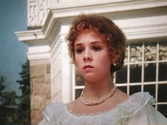 a woman in a white dress and pearls on her necklace is looking at the camera