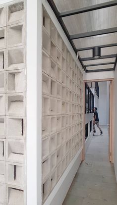 a man walking down a hallway next to a white wall covered in blocks and bricks