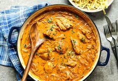 a blue pot filled with chicken curry next to a bowl of pasta and silverware