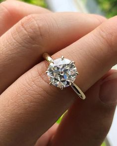 a woman's hand holding a ring with a white diamond in the middle and yellow gold band