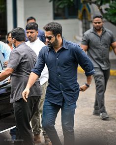 a man in blue shirt and black pants walking next to other men on the street