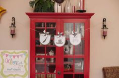 a red china cabinet with baby shoes hanging from it's front and side doors