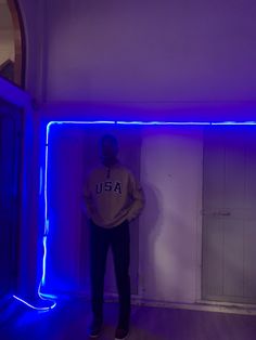 a man standing in front of a wall with blue neon lights on it and his hands in his pockets