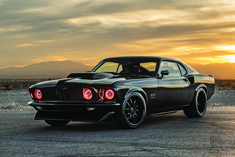 a black muscle car parked on top of a parking lot with the sun setting in the background