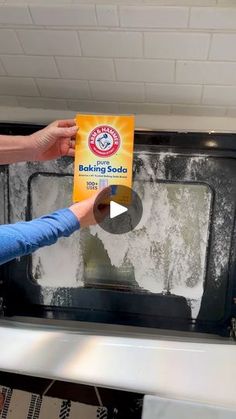 a woman holding up a box of baking soda in front of an open oven door