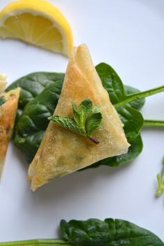 two pieces of food on top of green leaves and lemon wedges with one slice cut in half