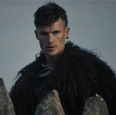 a man with long black hair wearing a fur coat and holding two large rocks in front of him