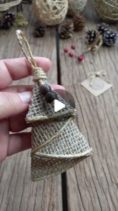 someone is holding a small christmas tree ornament on a wooden table with pine cones and other decorations