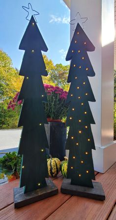 two wooden christmas trees with lights on them sitting on a porch next to a potted plant