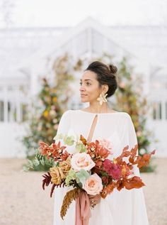 a woman holding a bouquet of flowers in her hand and wearing a white dress with an orange sash