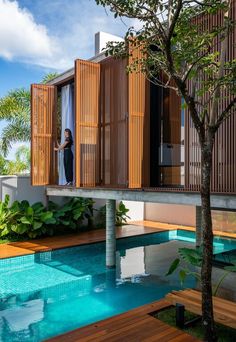 a woman standing on the balcony of a house next to a swimming pool and trees