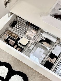 an open drawer with makeup and other items in it on the floor next to a rug