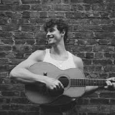 a man holding a guitar in front of a brick wall