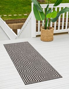 a black and white rug sitting on top of a wooden floor next to a potted plant