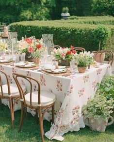 a table set up with flowers and plates on it in the middle of some grass