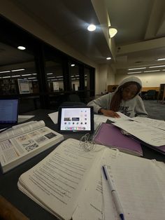 a woman sitting at a table with books and papers on top of her laptop computer