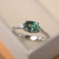 a green ring sitting on top of a white box next to a pair of diamonds