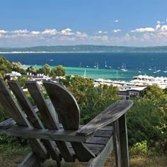 a wooden bench sitting on top of a lush green hillside next to the ocean with boats in the water