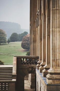 an old building with columns and a clock on the front wall, overlooking a grassy field