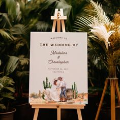 an easel with a wedding sign on it in front of some potted plants