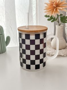 a black and white checkerboard coffee cup next to a flower in a vase