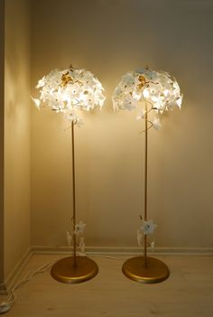 two floor lamps with flowers on them in a corner next to a white wall and wooden floor