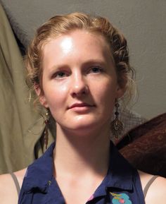 a woman with blonde hair and blue shirt posing for a photo in front of a wall