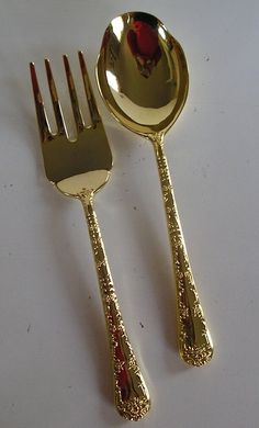 two gold colored forks and spoons on a white surface with a red rose in the center