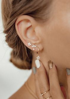 This set consists of four separate earrings, in three different styles, all made from 18 karat gold-plated sterling silver and embellished with zirconia stones. It has: 🌟 One stud earring with four tiny zirconia arranged in a flower shape; 🌟 One stud earring with three marquise-cut zirconia arranged in a fan shape with one small round zirconia hanging beneath; 🌟 One pair of huggie hoop earrings with a flower shaped charm hanging from their lower edge, decorated with six round zirconia. A femi