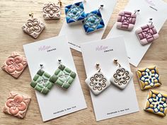 four different colored earrings sitting on top of a wooden table next to cards with the same design