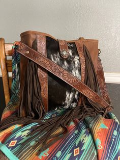 This large tote bag has a gorgeous leather strap adorned with sunflowers that matches the leather accents on the bag. This smooth finished dark leather pairs nicely with the cowhide panel in the front middle. The bag features both a zipper closure and magnetic closure, as well as a zippered pocket on the back. This bag measures 15.5" wide and 13" tall.  Please note all hides vary so the pattern may not be exactly as shown. The initial listing is for a Sedona bag only, but now you have the option Feather Purse, Purse With Fringe, Western Tote Bags, Personalized Purse, Western Bag, Hippie Purse, Cowhide Purse, Concealed Carry Purse, Western Purses