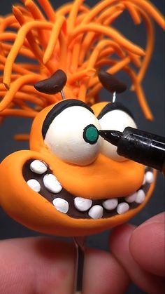 a hand holding a small orange toy with eyes and teeth