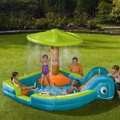 children playing in an inflatable pool with a water fountain and umbrella on the lawn