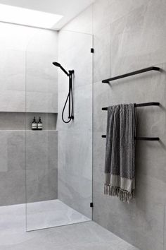 a bathroom with a shower, towel rack and glass door that has black handles on it