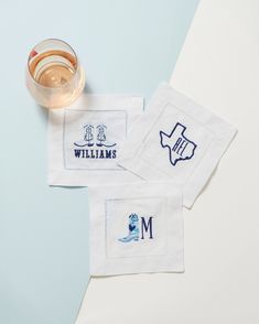 two embroidered napkins sitting on top of a table next to a glass of water