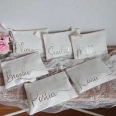 six embroidered name tags on white fabric with pink roses in the corner and lace around them