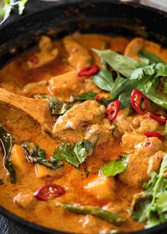 a skillet filled with chicken and vegetables on top of a wooden spatula next to a green leafy garnish